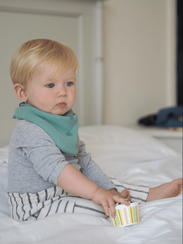 Boy model wearing Sage dribble bib on bed
