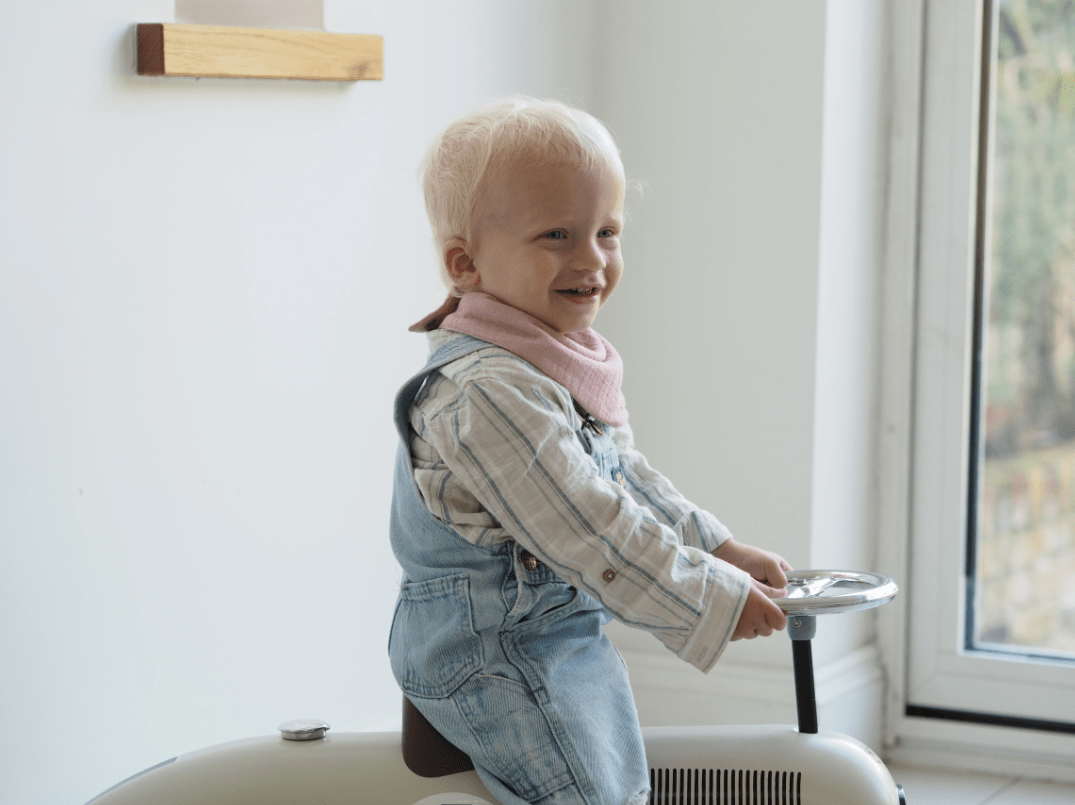 Boy model wearing Dusty Pink dribble bib riding toy car