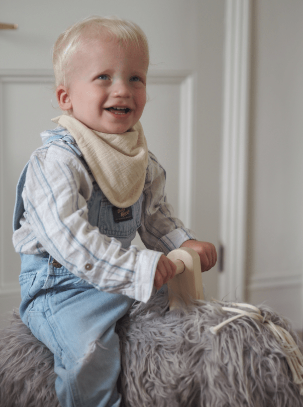 Boy model wearing Oat colour bib riding mammoth toy